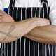 Close-up of chef's crossed arms, one of which has whisk and knife tattoos